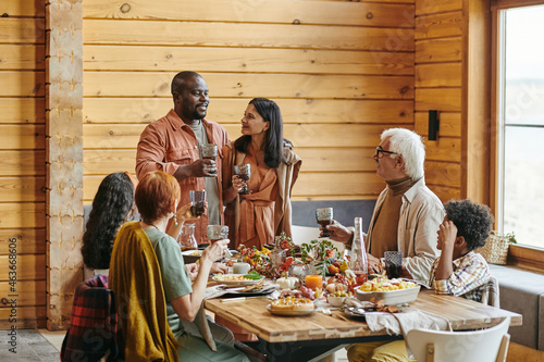 African young couple holding glasses with wine and saying the toast for their family at the table