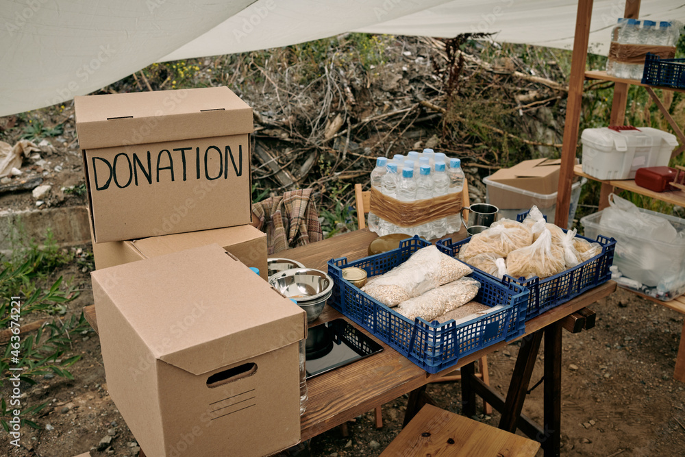 Packed boxes with clothes and donation food on wooden table in large