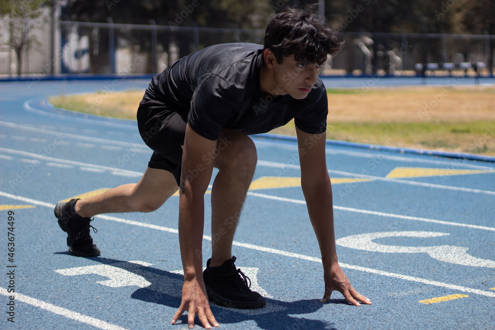 Runner ready in the starting area of a running track, looking straight ahead with determination Runner ready in the starting area of a running track, looking straight ahead with determination