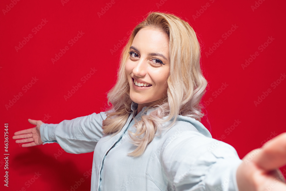 Selfie. Close up pleased beautiful girl takes photo of himself with her smartphone, isolated on red background. Focus on face Selfie. Close up pleased beautiful girl takes photo of himself with her smartphone, isolated on red background. Focus on face