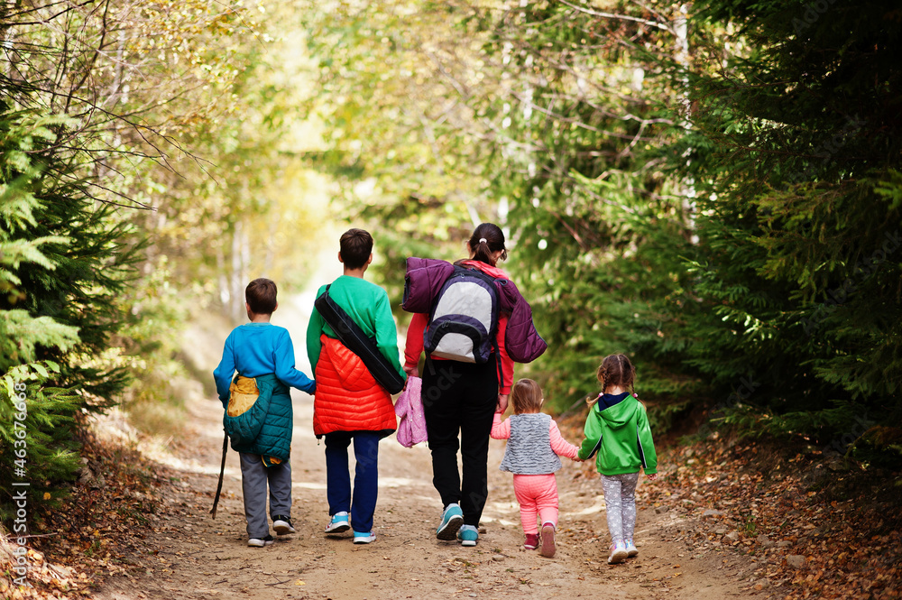 Back of mother with four kids walking on wood mountains. Family travel and hiking with childrens. Wear backpack. Back of mother with four kids walking on wood mountains. Family travel and hiking with childrens. Wear backpack.