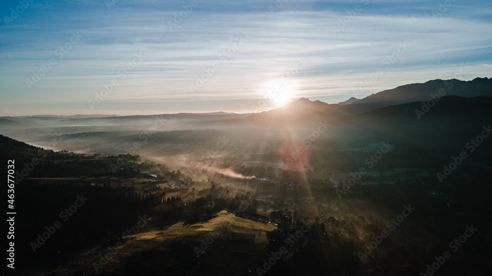 Scenic sunset at mountain range silhouette aerial view. The first or last rays of the sun. Mountains sunrise in the foggy morning above at mountain valley from drone.