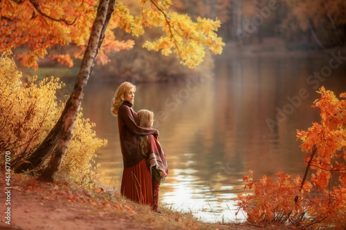Mother and daughter in the autumn park looking at the lake