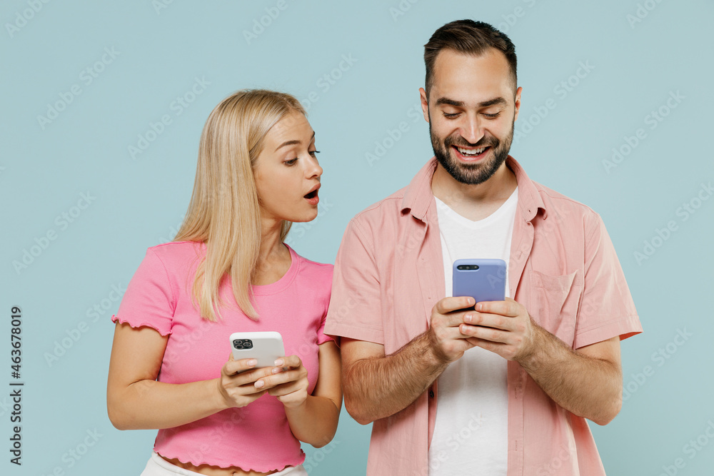 Young couple two friends family man woman in casual clothes hold in hand use mobile cell phone peeps together isolated on pastel plain light blue background studio portrait People lifestyle concept. Young couple two friends family man woman in casual clothes hold in hand use mobile cell phone peeps together isolated on pastel plain light blue background studio portrait People lifestyle concept.