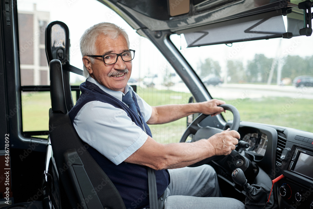 Happy aged driver of intercity bus holding by steering wheel during ride to another city or town - obrazy, fototapety, plakaty 