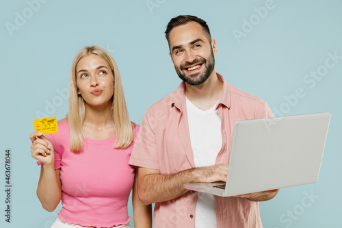 Young minded couple two friends family man woman in casual clothes use laptop pc computer credit bank card shopping online booking tour together isolated on pastel plain light blue background studio.