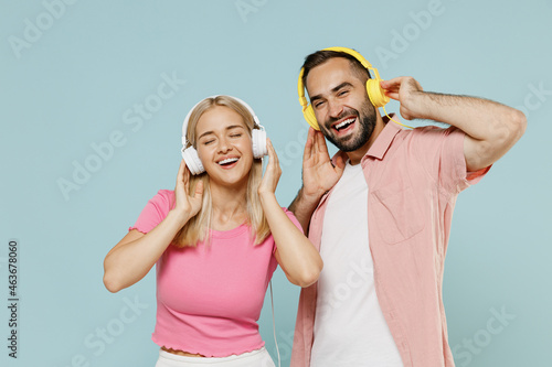 Young smiling happy couple two friends family man woman in casual clothes headphones listen to music together isolated on pastel plain light blue background studio portrait People lifestyle concept.
