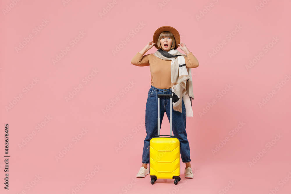 Full size body length traveler tourist shocked mature elderly senior woman 55 years old wears casual clothes hat scarf hold suitcase bag isolated on plain pastel light pink background studio portrait. Full size body length traveler tourist shocked mature elderly senior woman 55 years old wears casual clothes hat scarf hold suitcase bag isolated on plain pastel light pink background studio portrait.