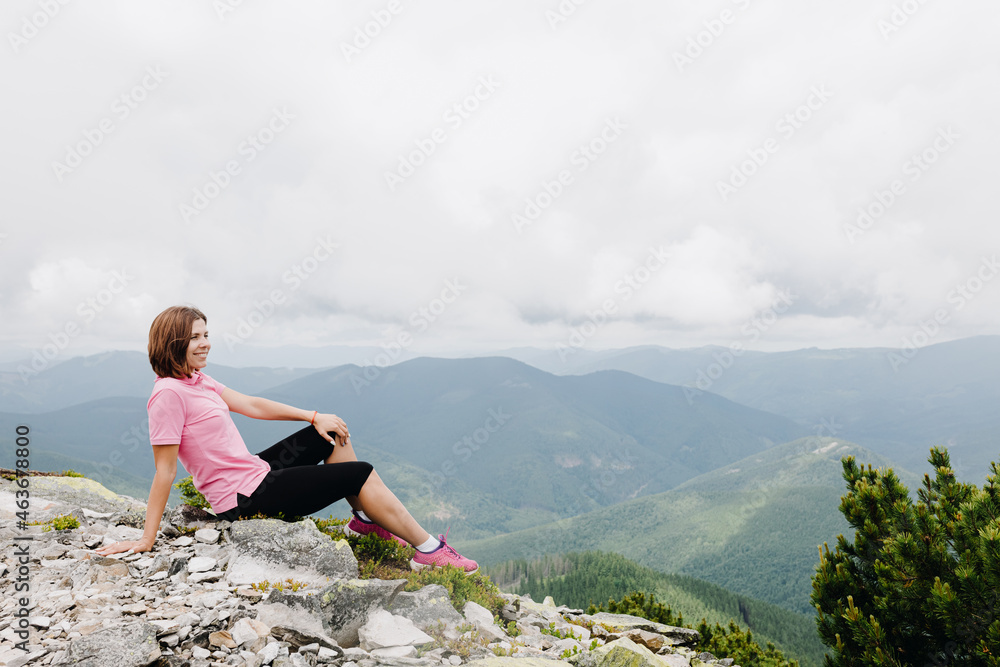 The girl sits on the top and admires the beautiful view of the Carpathian mountains, Ukraine.