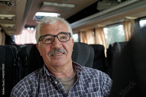 Face of mature male passenger in eyeglasses and shirt sitting on one of seats inside bus