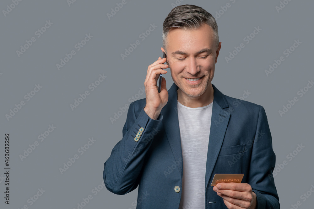 Man with smartphone near ear looking at credit card Man with smartphone near ear looking at credit card