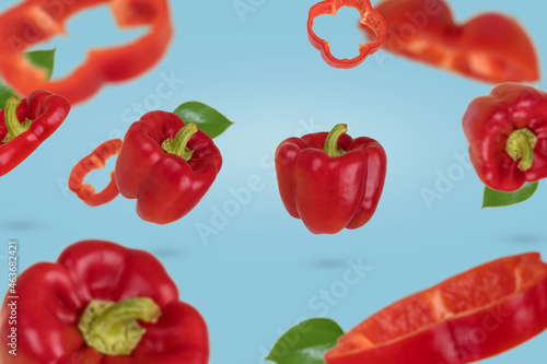 Fresh ripe whole and sliced red bell peppers flying in air isolated on a blue background. Healthy food, diet, vitamins, trendy food product.