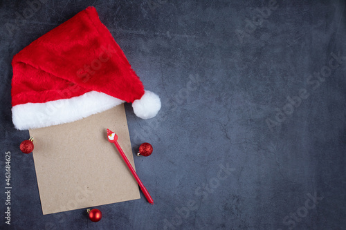 A sheet of craft paper with a red Christmas cap and a pen with Santa. Letter to Santa Claus. Preparations for the new year, space for text, dark background. Concept creativity, Christmas.