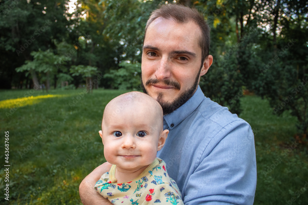 Dad and his little son are happy and looking at camera close-up. Father holding his baby son on the background of a summer landscape. Dad and his little son are happy and looking at camera close-up. Father holding his baby son on the background of a summer landscape.