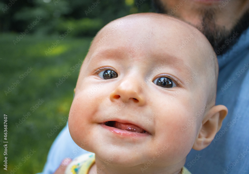 Baby boy looking at the camera and smiling close-up. Dad holds his newborn son in his arms outdoors. Baby boy looking at the camera and smiling close-up. Dad holds his newborn son in his arms outdoors.