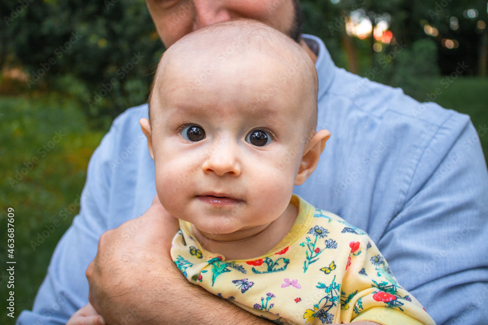Dad holds his baby son in his arms close-up outdoors. Kid looking at the camera. Father and his newborn son on the background of a summer landscape Dad holds his baby son in his arms close-up outdoors. Kid looking at the camera. Father and his newborn son on the background of a summer landscape
