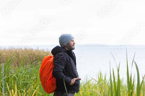 Man with orange backpack hiking by the lake