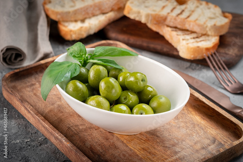 Large green ripe olives in a white bowl on a wooden table. Pickled olives with toast for breakfast