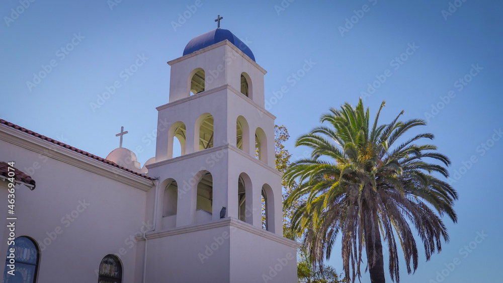 Small stucco Catholic church with bell tower surrounded by palm trees in sunny beach town on the Pacific Ocean coast
