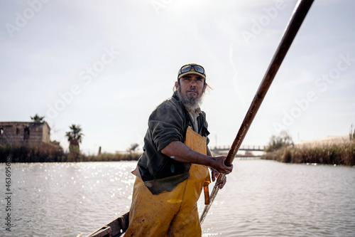 Front view of a fisherman standing in a boat using a push pole  photo