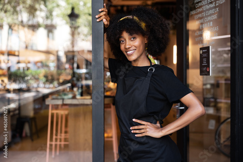 Smiling black waitress standing near entrance of cafe photo