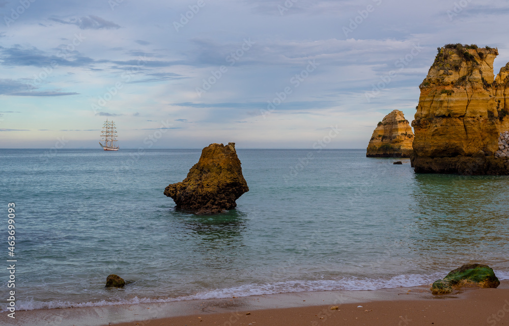 Pinhao Beach in Lagos Portugal in the evening with a sailing ship in the horizon.