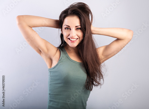 Happy laughing beautiful woman with epilation armpits holding muscular healthy arms on the head on blue background and happy looking in green t-shirt. Portrait