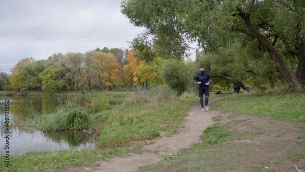 Young caucasian man running in park near pond on public autumn background, amateur runner jogging at outdoor workout on background of orange and yellow trees. Healthy lifestyle concept. Young caucasian man running in park near pond on public autumn background, amateur runner jogging at outdoor workout on background of orange and yellow trees. Healthy lifestyle concept.
