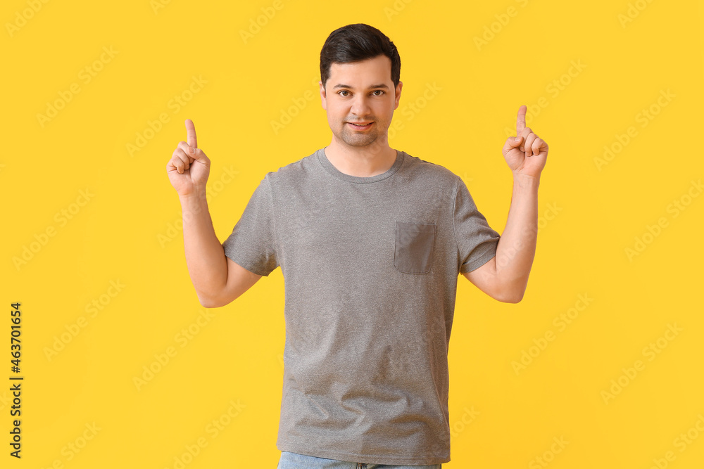 Handsome young man in stylish t-shirt pointing at something on color background Handsome young man in stylish t-shirt pointing at something on color background