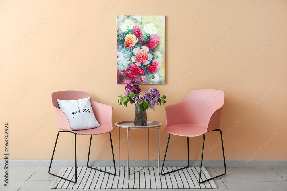 Fototapeta premium Modern pink chairs and glass vase with lilac flowers on table near color wall