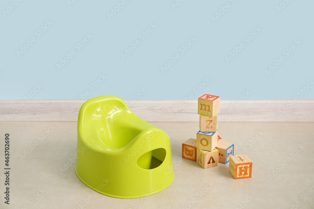 Fototapeta premium Potty and wooden cubes with letter on floor near color wall