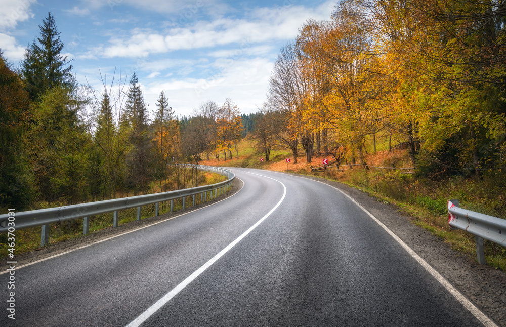 Road in autumn forest. Beautiful empty mountain roadway, trees with orange foliage and overcast sky. Landscape with asphalt road through the woods in fall. Travel in europe. Road trip. Transportation