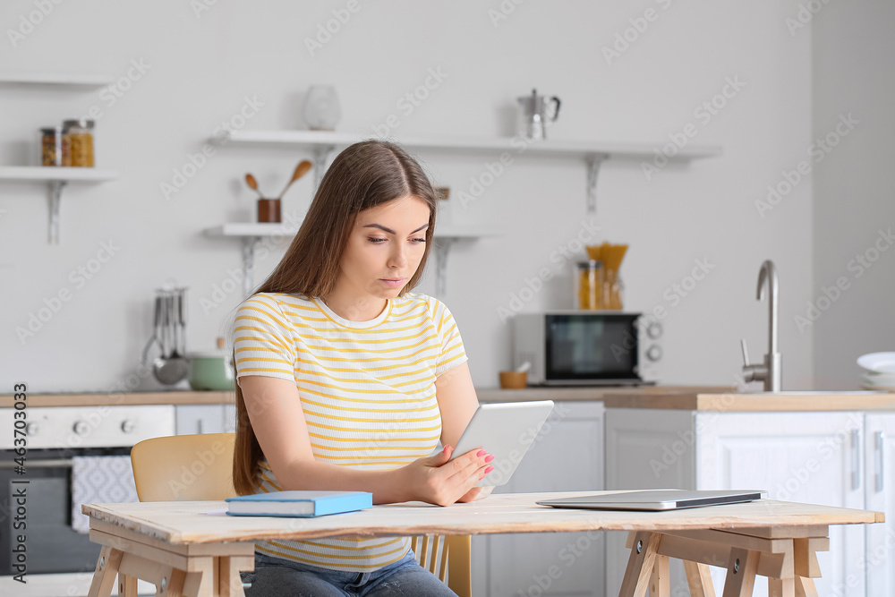 Young woman working with tablet computer at table in kitchen Young woman working with tablet computer at table in kitchen