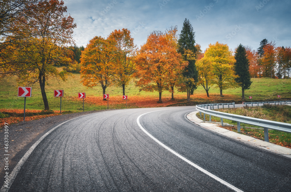 Obraz premium Road in autumn forest. Beautiful empty mountain roadway, trees with orange foliage and overcast sky. Landscape with asphalt road through the woods in fall. Travel in europe. Road trip. Transportation