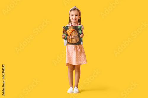 Cute little girl with book on yellow background