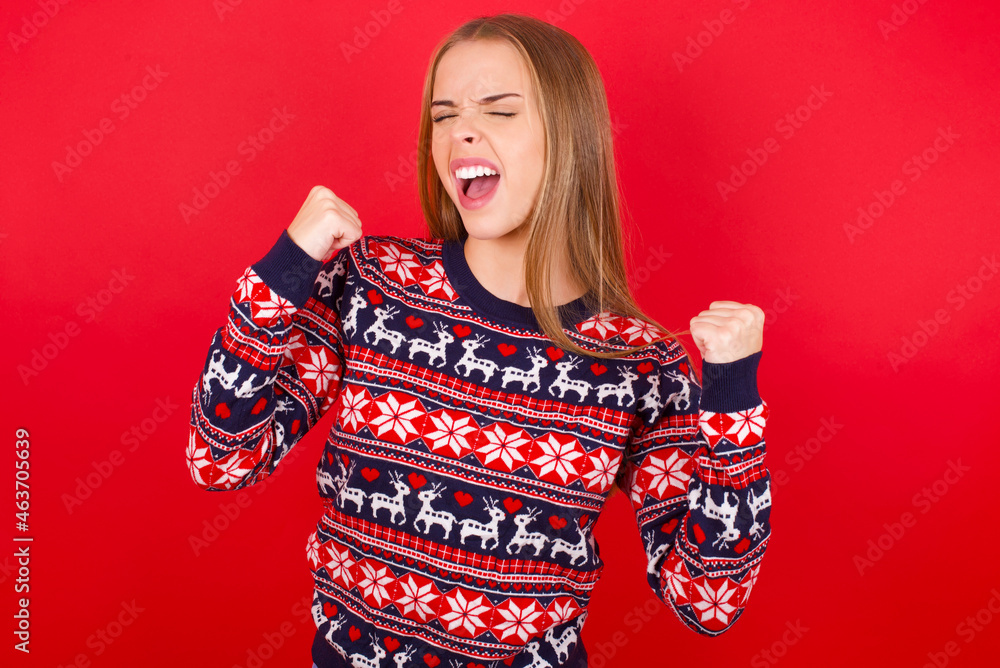 Young caucasian girl wearing christmas sweaters on red background celebrating surprised and amazed for success with arms raised and eyes closed. Winner concept. Young caucasian girl wearing christmas sweaters on red background celebrating surprised and amazed for success with arms raised and eyes closed. Winner concept.