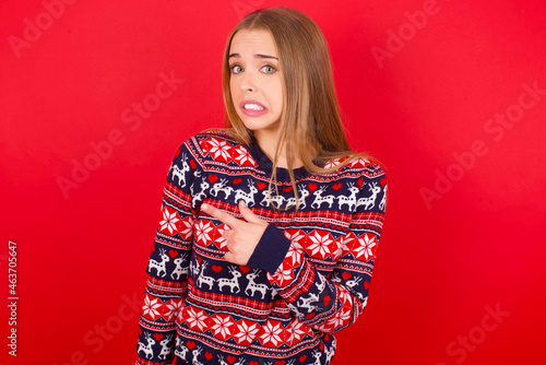 Young caucasian girl wearing christmas sweaters on red background Pointing aside worried and nervous with forefinger, concern and surprise concept.