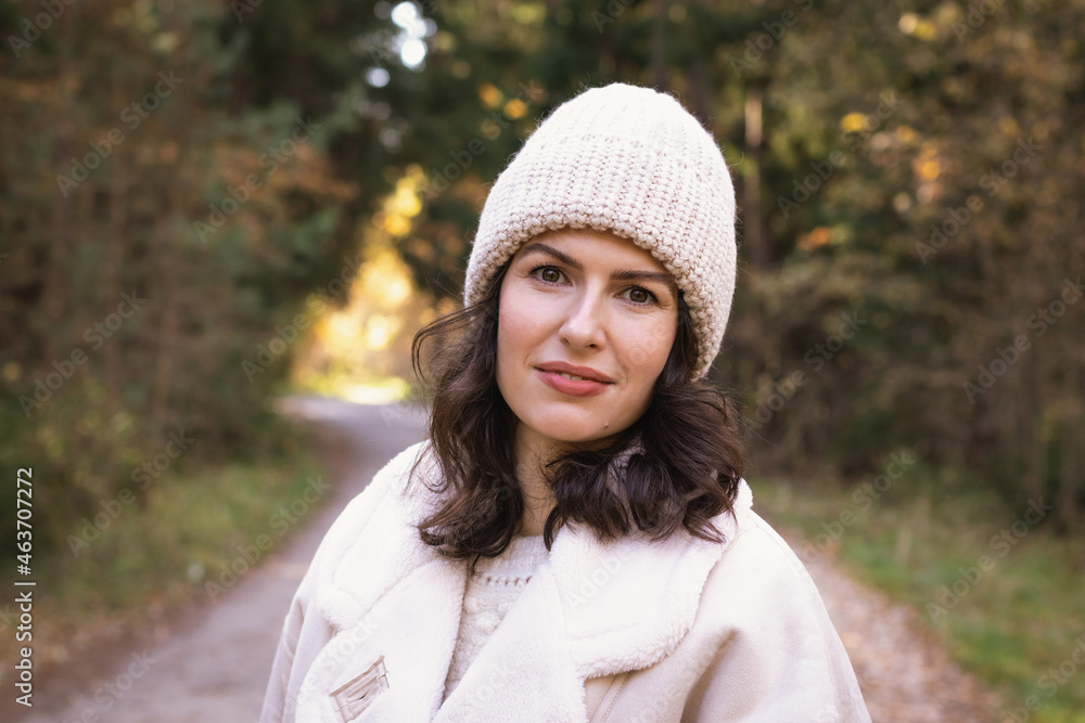 Portrait of a young brunette woman in a knitted hat and white jacket in the autumn forest Portrait of a young brunette woman in a knitted hat and white jacket in the autumn forest