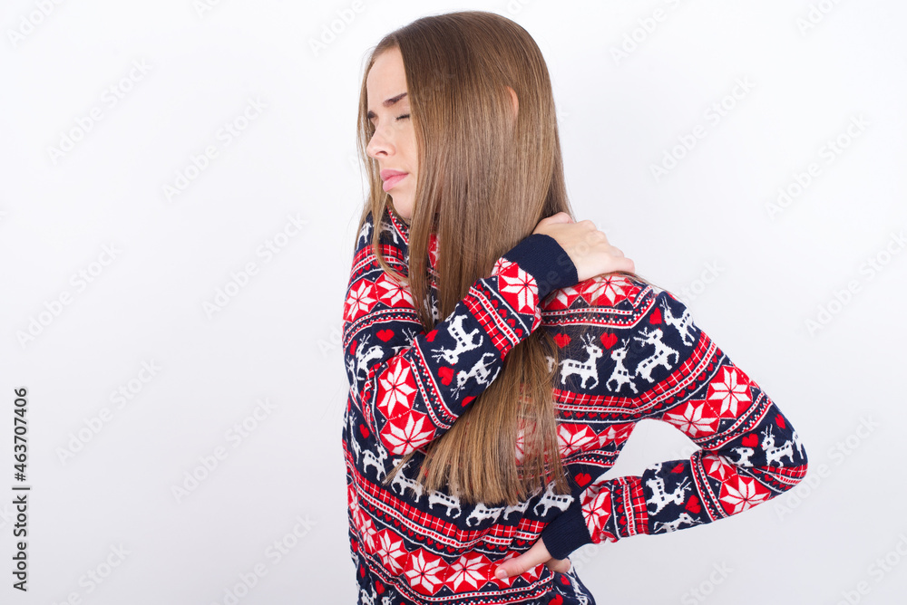 Young caucasian girl wearing christmas sweaters on white background got back pain Young caucasian girl wearing christmas sweaters on white background got back pain