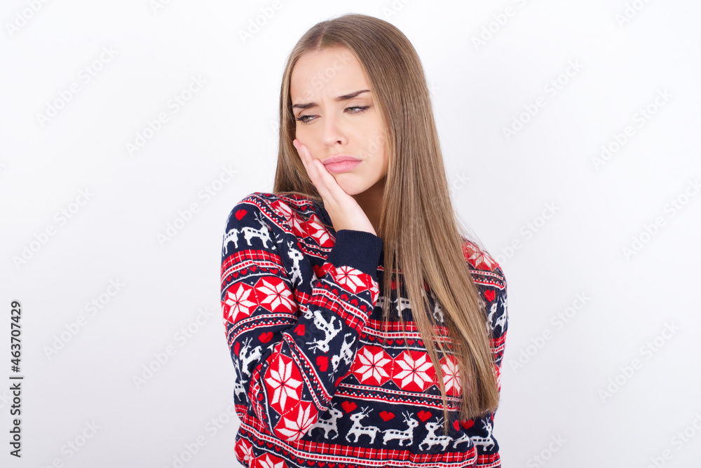 Young caucasian girl wearing christmas sweaters on white background with toothache Young caucasian girl wearing christmas sweaters on white background with toothache