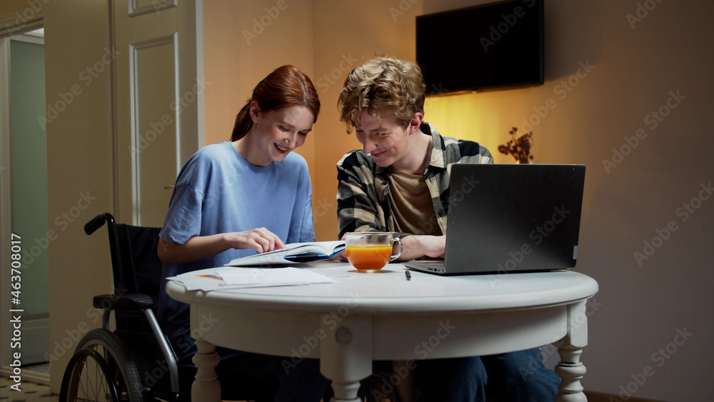 A disabled girl is reading a book while her friend is looking for something on the Internet A disabled girl is reading a book while her friend is looking for something on the Internet
