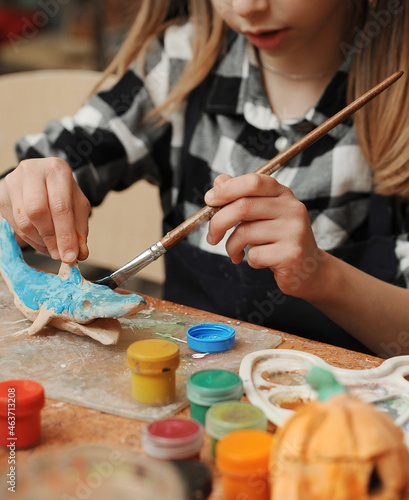 A little girl paints a clay product