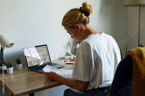 Young woman reading papers near laptop photo