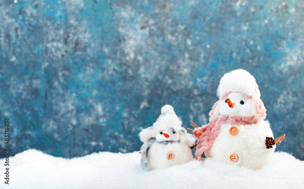 Christmas and new year snow concept with two cute snowmen in hats and scarves in snowdrift on blue background Christmas and new year snow concept with two cute snowmen in hats and scarves in snowdrift on blue background