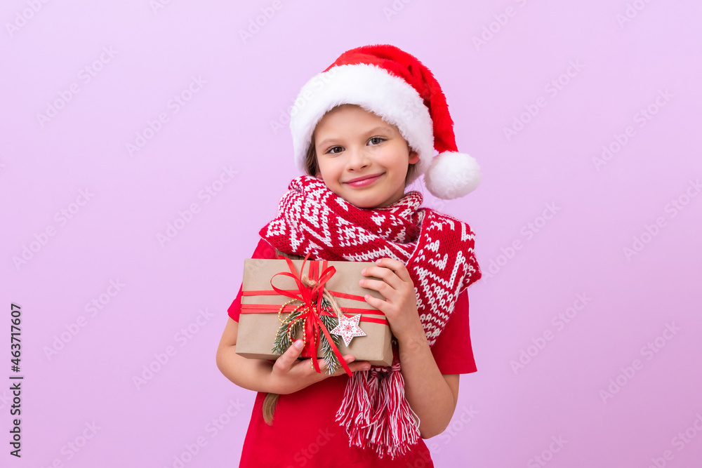 A little girl in a red Christmas scarf and a festive hat holds her Christmas gift and smiles. A little girl in a red Christmas scarf and a festive hat holds her Christmas gift and smiles.