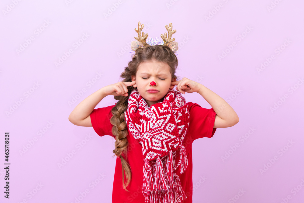 A little girl in a Christmas reindeer outfit and with a warm scarf put her fingers in her ears and closed her eyes. A little girl in a Christmas reindeer outfit and with a warm scarf put her fingers in her ears and closed her eyes.