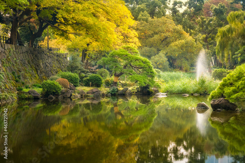 Fototapeta Naklejka Na Ścianę i Meble -  Beautiful and peaceful nature corner with a fountain and reflectons in the pond's water in autumn at Hibiya Park in Chiyoda City, Tokyo, Japan.