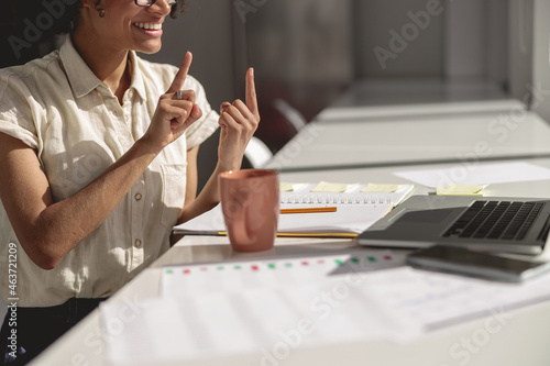 Smiling young lady learning and communicating in sign language online while sitting at workplace photo