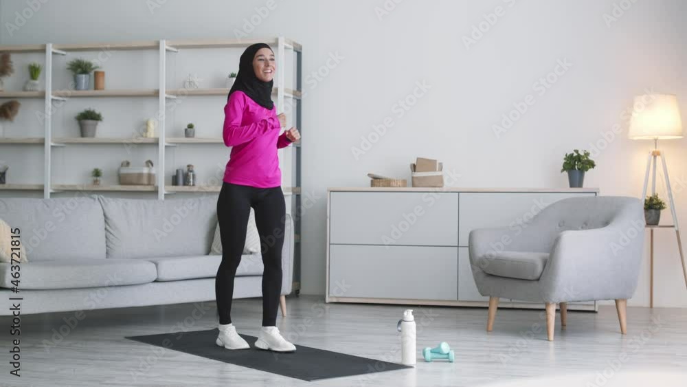 Dynamic fitness at home. Young happy muslim lady wearing hijab practicing active lunges and smiling Dynamic fitness at home. Young happy muslim lady wearing hijab practicing active lunges and smiling