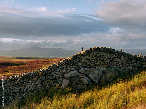 Ingleborough and drystone wall built over large rocks at sunset photo